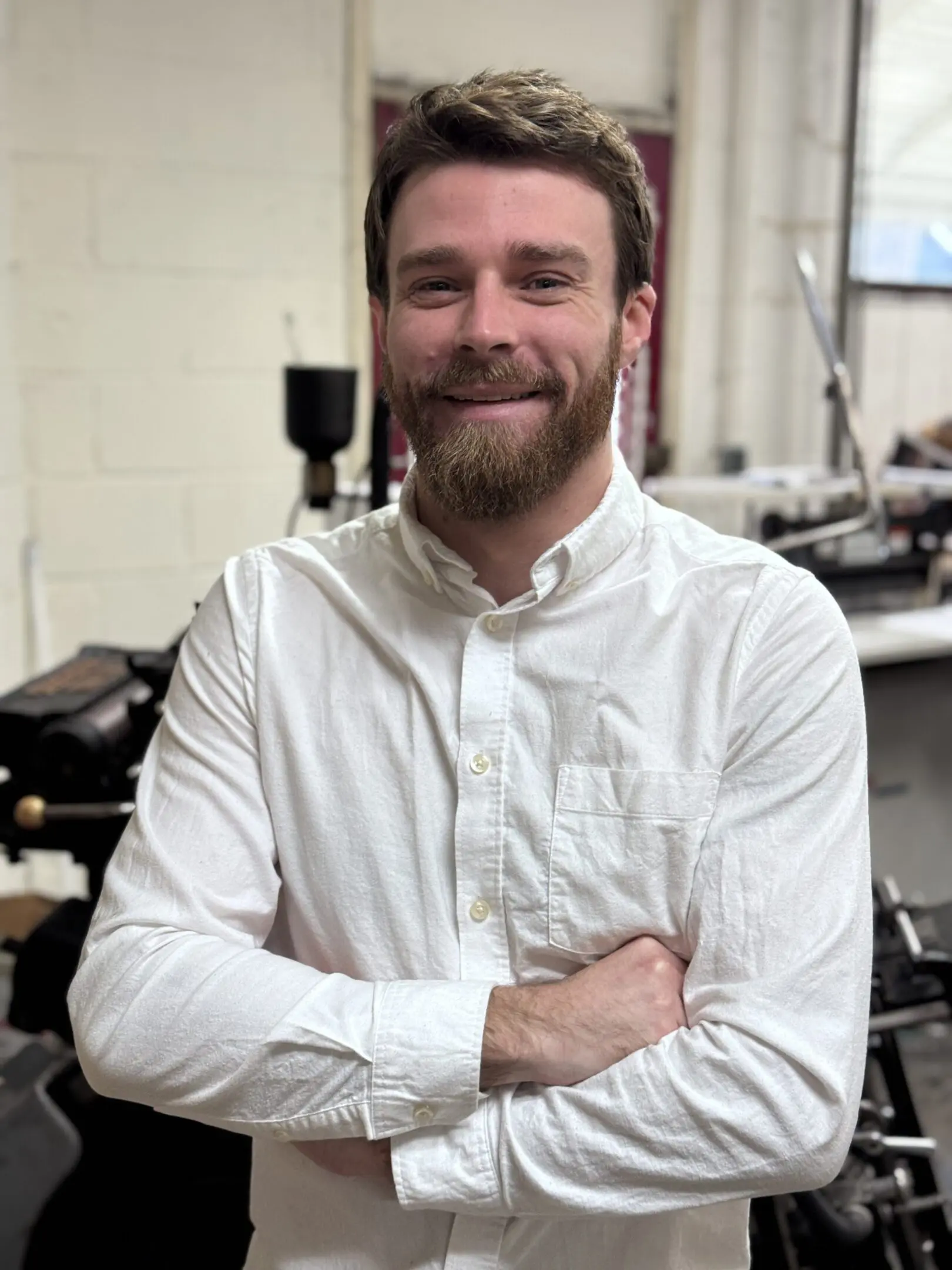 Man in white shirt with beard smiling, arms crossed.