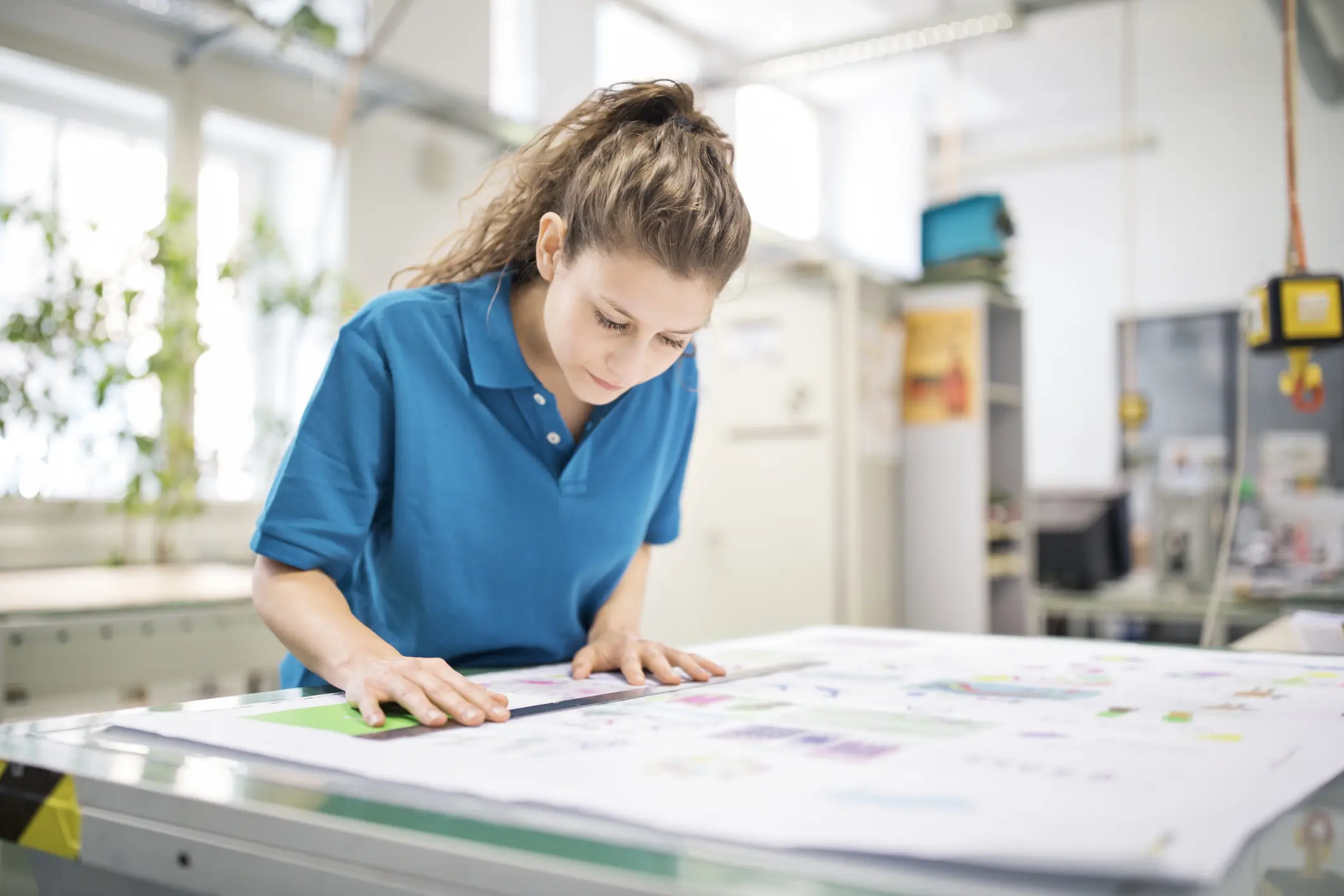 A young woman focused on drawing architectural plans in a bright studio.
