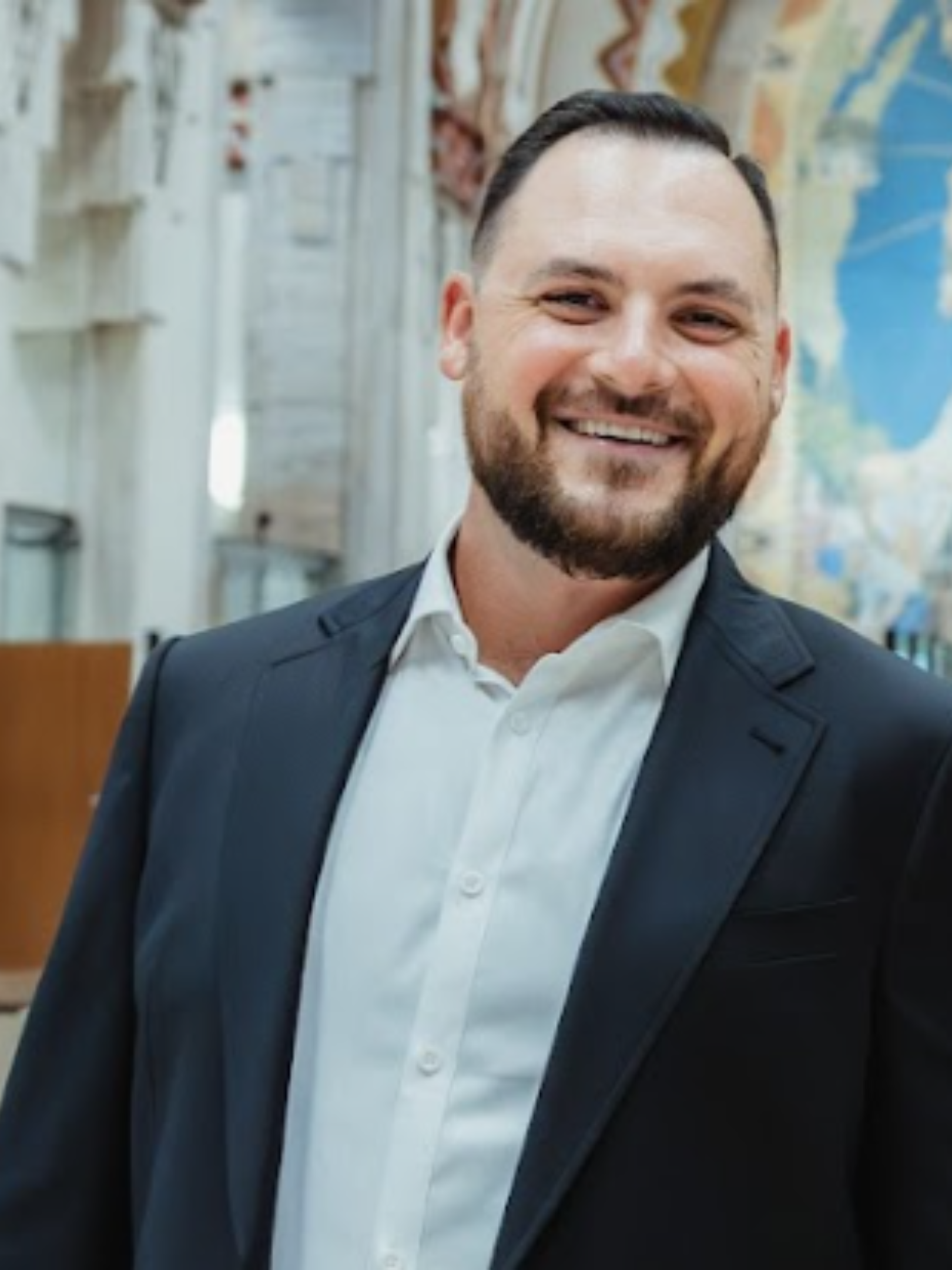 Smiling man in a suit jacket and white shirt outdoors.