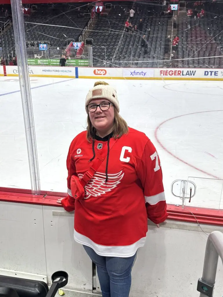 Person in a red Detroit Red Wings hockey jersey at an ice rink.